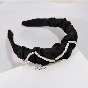 Détail d'un serre-tête en tissu plissé noir avec des perles blanches style vintage