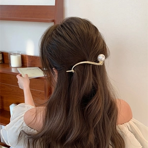 Dettaglio dell'elegante fermaglio dorato a onda con grande perla sui capelli mossi