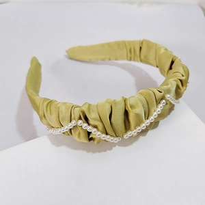 Détail macro du serre-tête en satin plissé doré avec bordure en perles élégantes