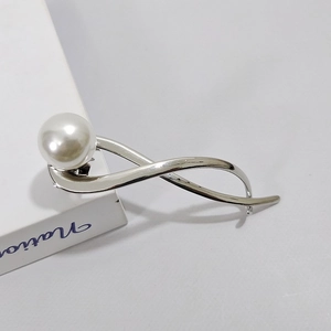 Dettaglio della molletta in metallo argento con design a spirale lucida e perla bianca