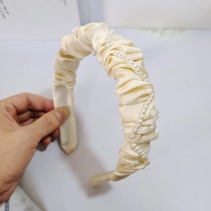 Détail d'un serre-tête plissé crème avec perles blanches et structure interne élastique