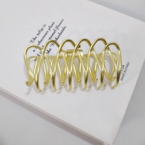 Macro detail of matte gold metal hair claw clip with wavy texture on white book
