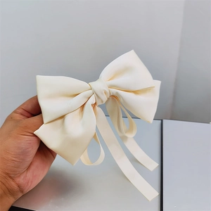 Close-up of cream satin bow hair clip with long ribbons held in hand for detail