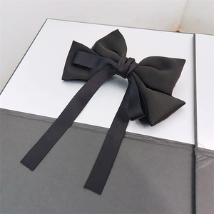 Elegant black satin bow hair clip with long ribbons on a modern minimalist display case
