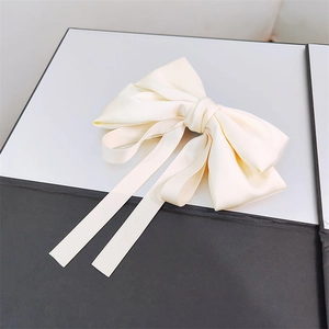 Detail view of the elegant cream satin bow hair clip with flowing ribbons and silky texture