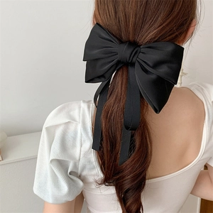 Detail showing elegant black satin bow hair clip with long flowing ribbons on model