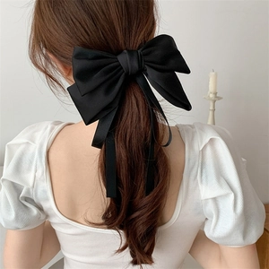 Detail showing elegant black satin bow hairclip with long ribbons on model's hair