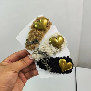 Three plush hair bands in khaki, white, and black with gold heart and Smile details