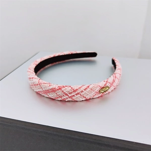 Close-up of pink and white tweed headband with golden metal tag and woven texture