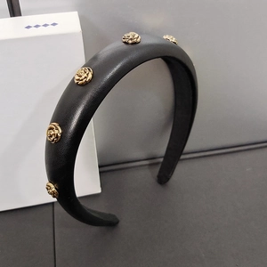 Close-up of black leather headband with five golden roses against a minimalist box