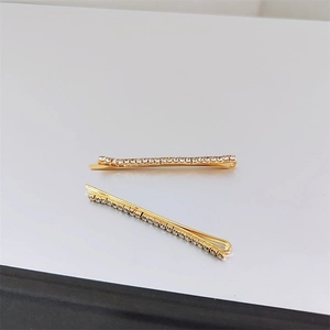 Detailed view of two gold-plated hair clips with sparkling rows of white rhinestones