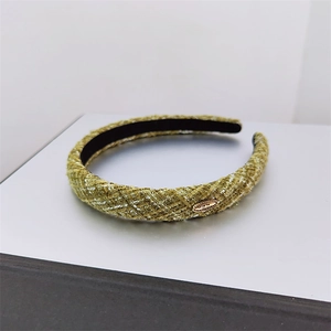 Detail of olive green tweed headband featuring a gold oval metal tag and soft inner lining