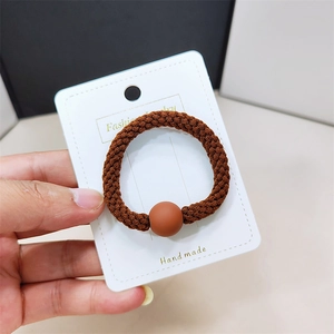 Élastique cheveux tressé marron avec perle mate sur carte pour un style minimaliste