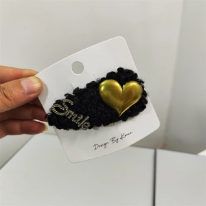 Detail showing a black fuzzy lamb wool heart clip with gold Smile rhinestone accents
