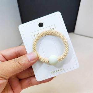 Détail d'élastique à cheveux beige tissé main avec perle verte mate sur carte