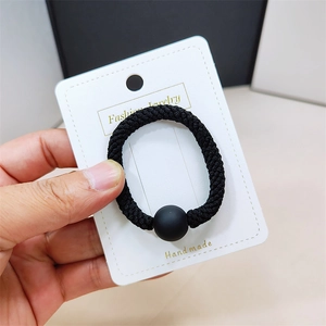 Gros plan d'un élastique à cheveux noir épais avec perle mate sur une carte