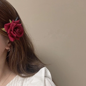 Elegante molletta per capelli con rosa di velluto rosso e foglie verdi sui capelli