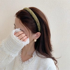 Detail of olive green tweed headband with metal logo plate and pearl earrings