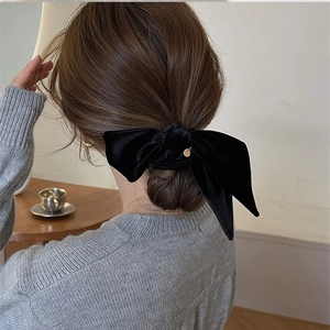 Detail of elegant black velvet bow hair scrunchie with a gold pendant worn on a bun hairstyle