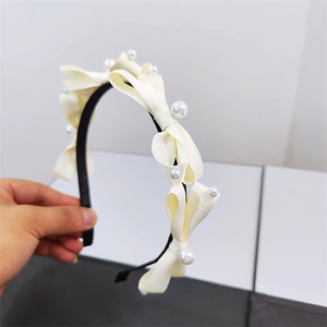 Detail of cream silk bow headband with white faux pearls and thin black band