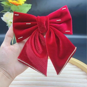 Detail of red velvet oversized bow hair clip with sparkling rhinestones and ribbed texture