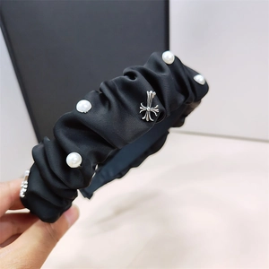 Detail of black pleated satin headband with pearls and vintage metal cross pendant
