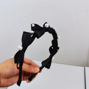Detailed close-up of a black satin bow headband with elegant white faux pearl accents