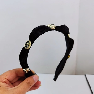 Elegant black velvet headband with gold floral charms and pearl accents shown in hand