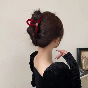 Detail of burgundy velvet camellia hair claw with golden rose center on model