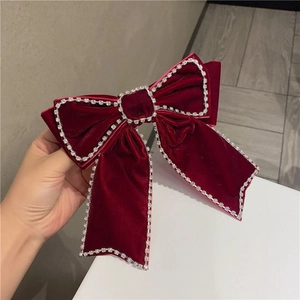 Close-up of a large red velvet bow hair clip with luxury rhinestone trim and long ribbons