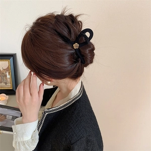 Detail view of a black velvet hair claw clip with a golden flower, worn by a model