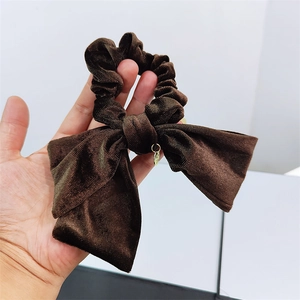 Detailed close-up of a brown velvet scrunchie with bow knot and golden charm detail