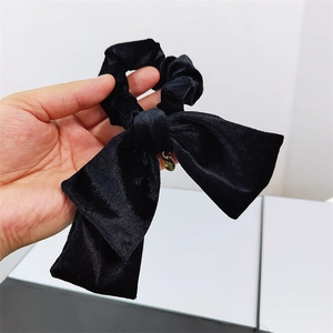 Detailed view of black velvet bow scrunchie with a round gold decorative metal tag