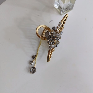 Détail d'une pince à cheveux dorée avec perles de cristal fumé et longs glands de chaîne