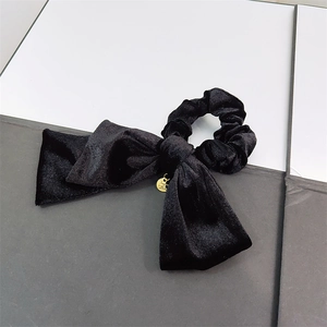 Detailed macro view of black velvet bow scrunchie with a gold metal pendant detail