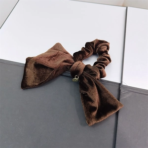 Detail of dark brown velvet bow scrunchie with elegant golden metal pendant charm