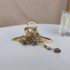 Détail d'une élégante pince à cheveux dorée avec perles en cristal gris et pompon pendant