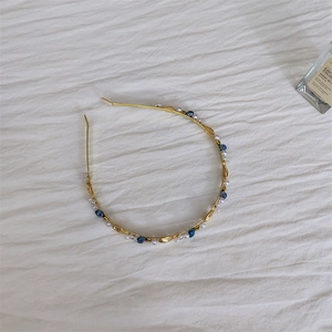 Detailed close-up of golden headband featuring white pearls and navy blue crystals