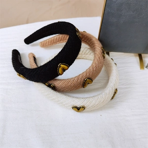 Close-up of three knitted headbands with vintage gold heart accents in black, beige, and khaki
