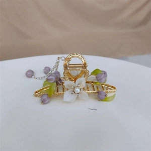 Detailed close-up of golden lily of the valley hair claw with pearl tassel on white platform
