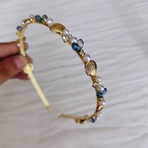 Detailed close-up of a gold headband with blue crystals, pearls, and metal seashells