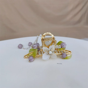 Detailed close-up of metal hair claw with white flower, purple lilies and pearl tassel