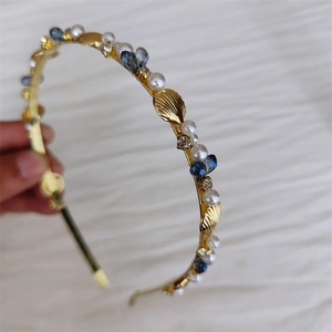 Detail of gold metal headband featuring white pearls, blue crystals and shell charms