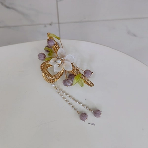 Close-up of golden orchid hair claw clip with purple lily pendants and pearl tassels