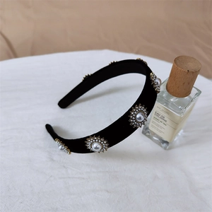 Détail d'un serre-tête en velours noir avec fleurs en perles et strass sur surface blanche