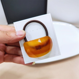 Handheld amber resin semi-circle hair ring with a brown elastic band on a display card