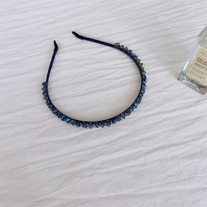 Détail d'un serre-tête bleu marine orné de cristaux facettés sur un tissu blanc texturé