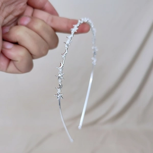 Detail of silver metal headband with stars, moons and pearls held by a hand