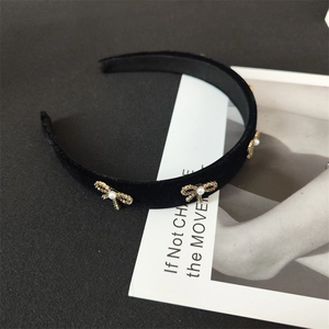 Detail of black velvet headband with golden crystal bows and white pearl accents