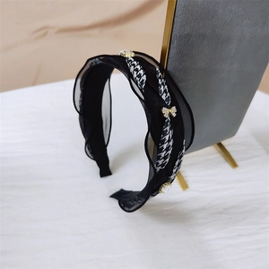 Detail of black fabric headband with lace trim, houndstooth ribbon, and golden rhinestone